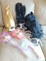 Photo of two packaged handheld pink/silver masquerade masks with glitter, five black and white masquerade masks with large black feathers, and one gold full-face mask with minor scratches.
