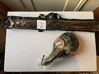Full view of the packaged long nose mask and folded metallic wings in carrying bag arranged on a white surface.