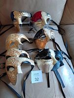 Seven assorted Phantom of the Opera style masks shown together on a sofa. Various colors and cracked texture with ornate detailing.