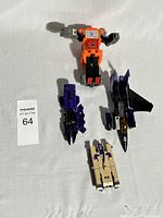 Four vintage Transformers figures displayed flat: orange robot, purple shuttle, smaller purple vehicle, tan and purple tank.