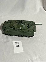 Full side view of green motorized MOBAT tank with visible treads and cannon barrel, set on white fabric background.