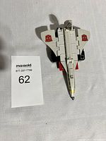 White and grey plastic jet toy viewed from top, showing yellow cockpit and red Autobot logos on wings.