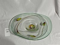 Clear art glass bowl with embedded colored swirls and floral motifs photographed from above on white fabric background.