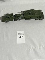 Full view of green cast metal military semi truck and trailer carrying a tank, showing the complete lot setup on a white surface.