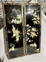 Full view of the two vertical black lacquer panels side by side showing mother of pearl inlay artwork depicting Asian figures and floral designs.