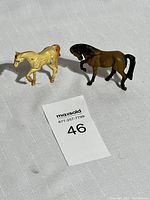 Two vintage cast iron horse figurines, brown and cream colors, placed on a white textured cloth