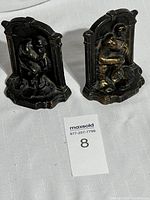 Pair of black and gold-toned solid brass bookends modeled after Rodin's The Thinker on a white surface with lot number card.