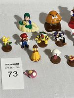 Overview of 10 Super Mario PVC figures including Luigi on cloud, Goomba, Waluigi, Bowser, Daisy, and others, arranged on white surface.