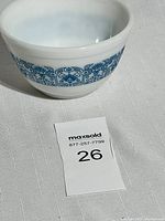 White opaque glass Pyrex mixing bowl with blue decorative Blue Horizon pattern band around the outside, shown on a white textured surface.