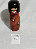 Vintage Japanese Kokeshi wooden doll on white textured surface showing full body and hair detail.