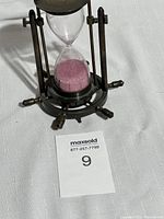 Front view of the vintage nautical hourglass with pink sand and brass frame on white fabric.