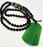 Full view of black beaded necklace featuring a green jade pendant and decorative smaller beads in green and amber near the clasp.