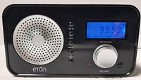Front view of a black Eton sound radio with blue-backed frequency display, volume knob, and function buttons.