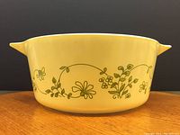 Yellow Pyrex casserole dish with green floral Shenandoah pattern, side view showing handle and design.