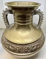 Front view of brass urn showing carved band of mythical creatures and one decorative handle