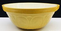 Side view of vintage bowl showing yellow exterior, embossed design and white interior interior.