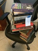 Stack of assorted books on a black office chair, showcasing multiple titles with focus on photography and history.
