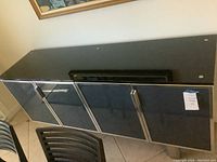 Full view of contemporary buffet showing black glass top, four black glass doors with metal frames and handles.