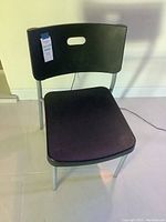 Single black plastic chair with metal legs, viewed from front angle showing seat, backrest with a handle cutout, and floor beneath.