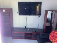 Frontal image showing the two tall cabinets flanking the low console beneath a wall-mounted TV. All pieces are wood finished with glass doors. The right console door does not fully close.