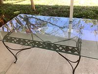 Top angle view of rectangular glass patio table showing clear glass surface and black metal frame with lattice design.