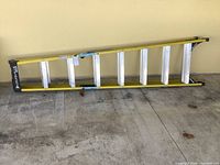 Full view of 8-foot fiberglass ladder laid flat against wall on concrete floor.