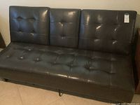 Full view of black leather-like futon sofa showing tufted seat and back cushions, metal legs, and general condition.