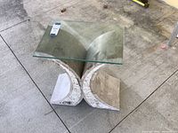 Full view of decorative table showing clear glass top and white marble-patterned sculptural base on a concrete floor.