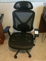Black mesh office chair showing front view with headrest, padded armrests, and casters on the base.