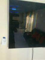 Samsung TV wall-mounted with some surrounding room visible in the reflection.