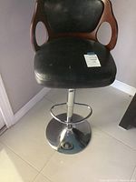 Front view of bar stool showing black leather-like seat, wooden backrest, and metal base with chrome finish.
