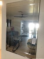 Full view of rectangular etched glass wall mirror hanging on wall, showing reflection of room and ceiling fan.