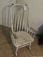 Front view of the white wooden rocking chair showing the curved backrest, seat, and armrests with worn paint.
