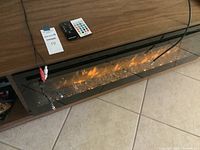 Close-up front view showing fireplace insert active, two remotes and RCA cables on top shelf