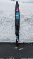 Full length view of waterski standing vertically on pavement with snow background showing complete ski and graphic design.