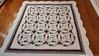 Full view of the quilt laid flat showing the interlocking ring patchwork and dark floral border on off-white background.