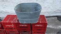 Side view of the metal wash tub showing its size and shape set on red crates with visible wear.