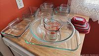 Collection of clear Pyrex glass dishes of various sizes stacked together with measuring cup and red lids.