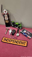 Photo showing full lot including model gas pump, green Kawasaki motorcycle, three watches, three costume rings, diecast race car model, and Independent patch.