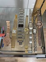 Photo of 10 assorted wristwatches with different styles and bands, displayed on a glass shelf.