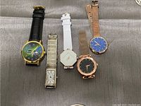 Four assorted wristwatches laid on grey fabric.