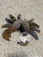 Photo of Ty Beanie Baby Claude the Crab plush toy lying on carpet, showing multicolored fabric, front claws, legs and attached heart tag.