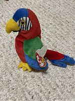 Photo of Ty Beanie Baby parrot stuffed toy named Jabber showing red, blue, green, yellow, and zebra-striped face with attached tag.