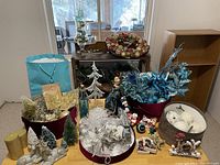 Overview of Christmas ornaments lot showing multiple items including reindeer figurines, artificial trees, wreath, crafting floral pieces, and various balls in baskets, along with candles and a 'joy' sign.