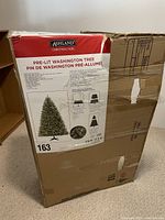 Box front showing Ashland brand, product name Pre-lit Washington Tree, product number 163, size 7.5 ft/2.2 m, and features including quick set technology, pre-attached hinged branches, natural branch tips, and tree stand included.