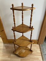 Front view of the wooden corner shelf with four triangular tiers and turned spindle supports.