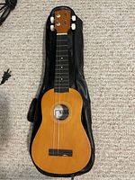 Full view of the ukulele on top of a black carrying case, showing the front side with tuning pegs and fretboard.