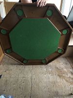 Octagonal wooden poker table top with green felt surface and eight circular cup holders displayed upside down