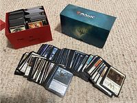 Cards in red box with many Magic The Gathering cards laid out on carpet floor showing diversity of cards.