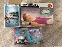 Photo of the boxed Pro Shiatsu neck massager and AirPress leg and foot massager products, showing packaging with promotional imagery and text.